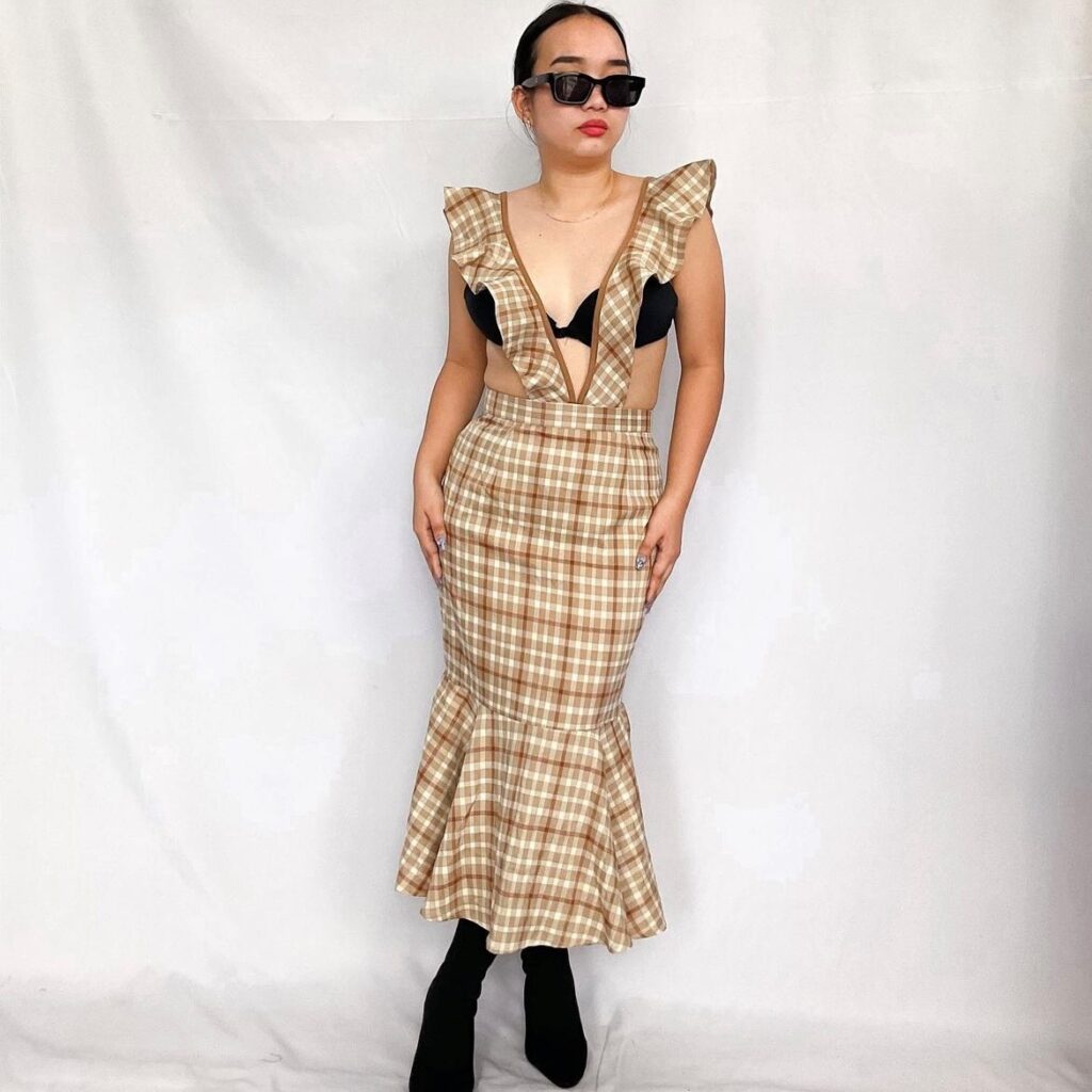 Woman wearing an example of flirty hemlines. A tan plaid dress with flared bottom. 