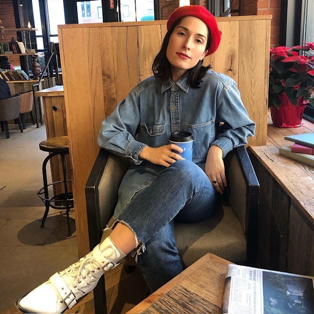 woman in coffee shop wearing a denim shirt, jeans, white boots, and a red beret