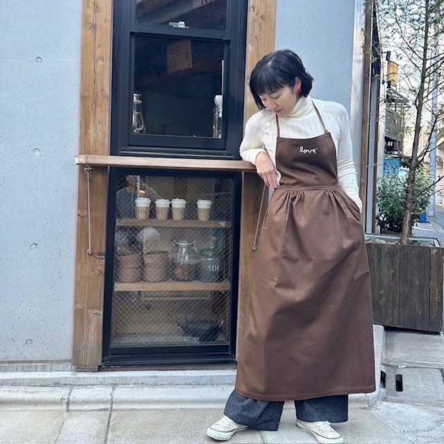 woman wearing a brown apron dress over a cream-colored turtleneck and jeans