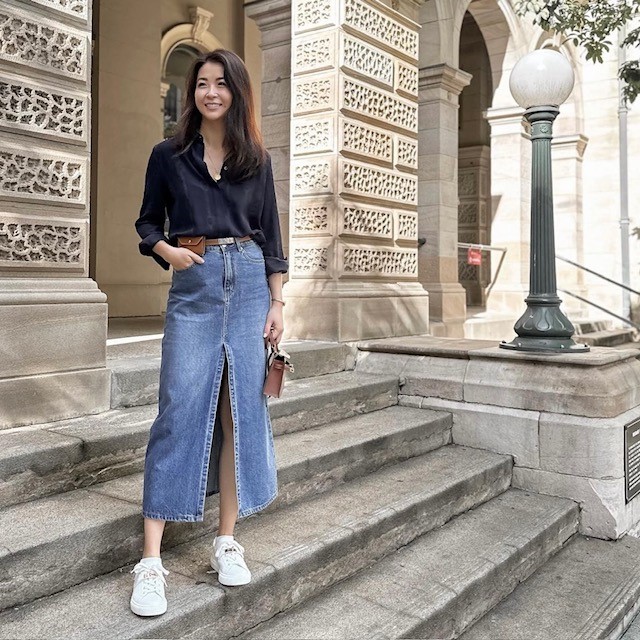 woman wearing a black blouse and sneakers with a long denim skirt