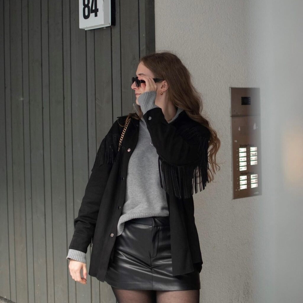 woman wearing a black jacket, gray sweater, and black leather skirt