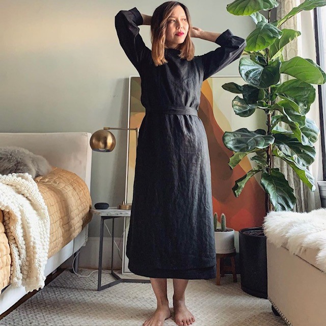 woman wearing a charcoal apron dress over a black blouse