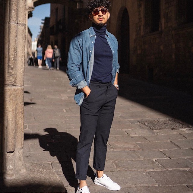 A man wearing an example of a casual New Year's Eve outfit, a navy blue turtleneck, black pants, and a denim buttondown