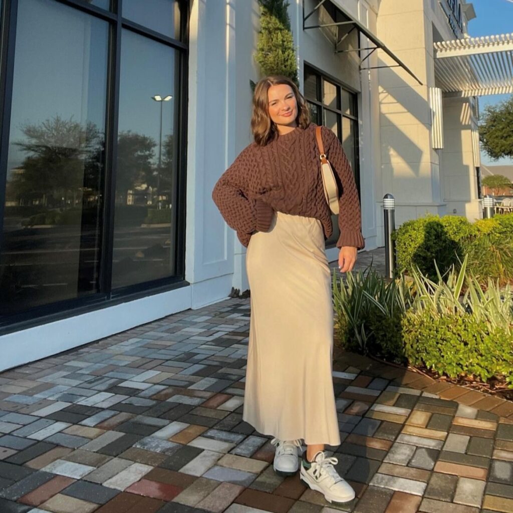 A woman wearing an example of a casual New Year's Eve outfit, a brown sweater and tan slip skirt with sneakers