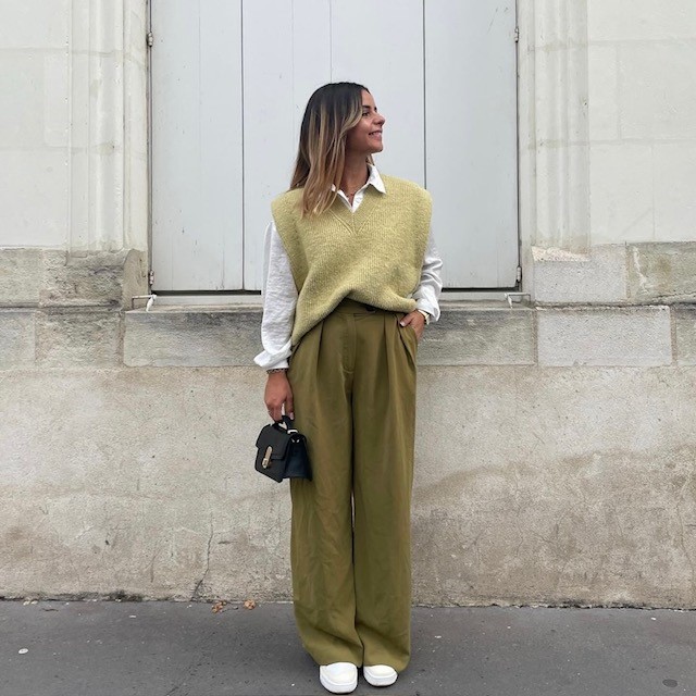 A woman wearing a light green sweater vest with oversized olive trousers and white sneakers