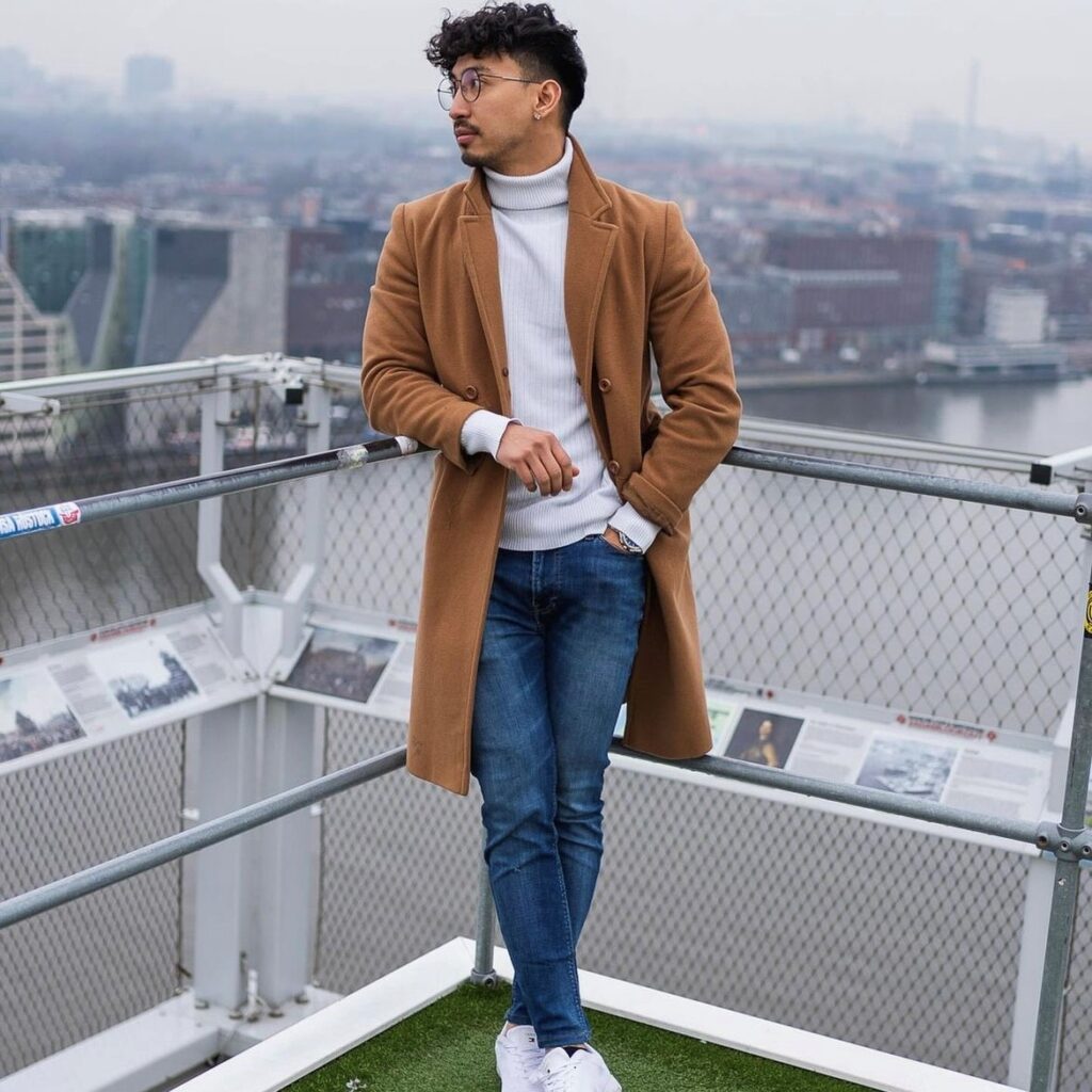 A man wearing a turtleneck and jeans with a camel coat