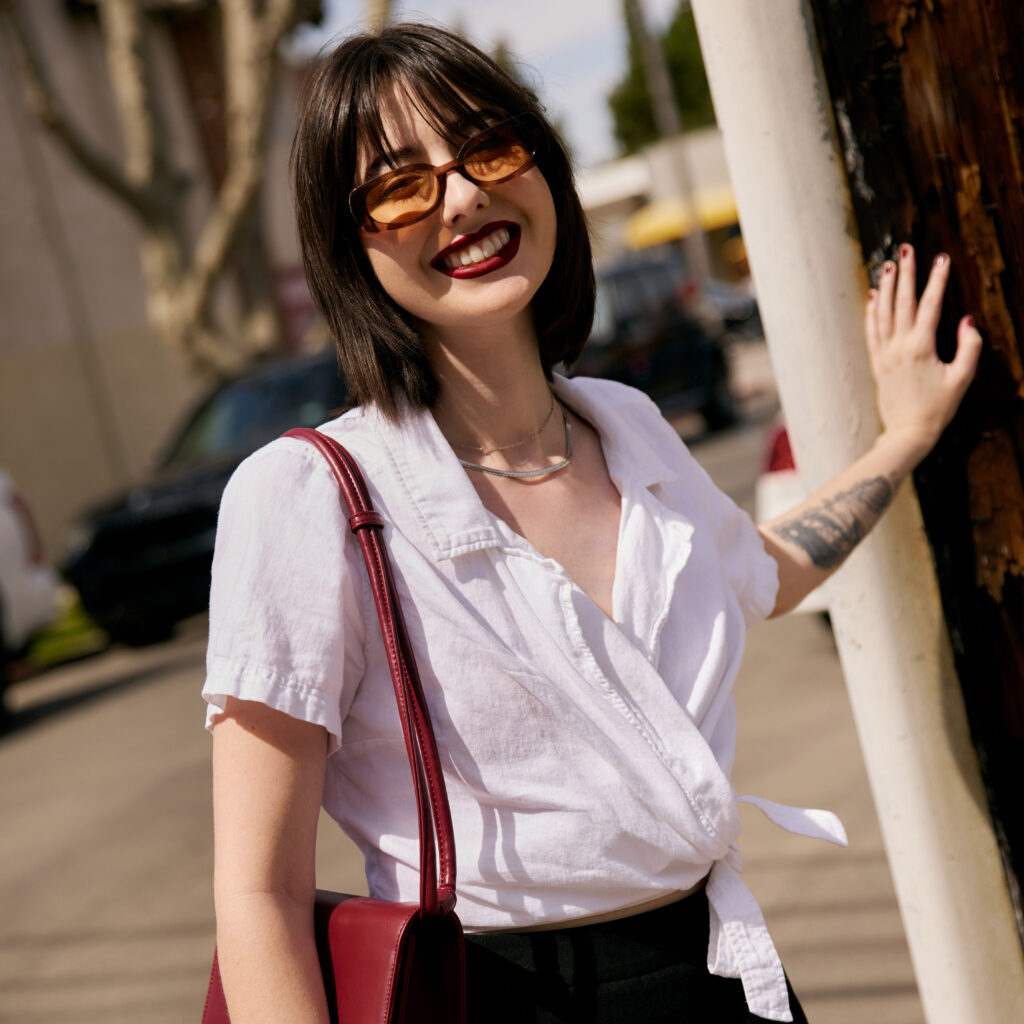 Cate wearing a white button up shirt and black skirt holding a red purse