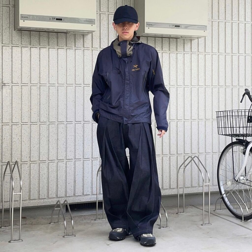 person wearing gorpcore fashion, a rain jacket with wide-leg trousers and a baseball cap