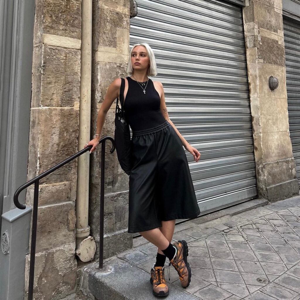 woman wearing gorpcore fashion with a black tank top, black a-line skirt, and hiking shoes