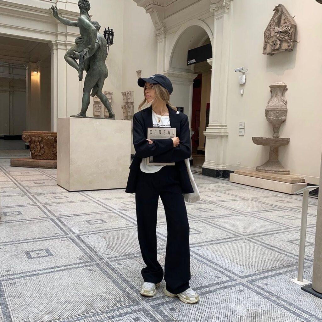 woman wearing a black oversized suit with trainers, t-shirt, and baseball cap