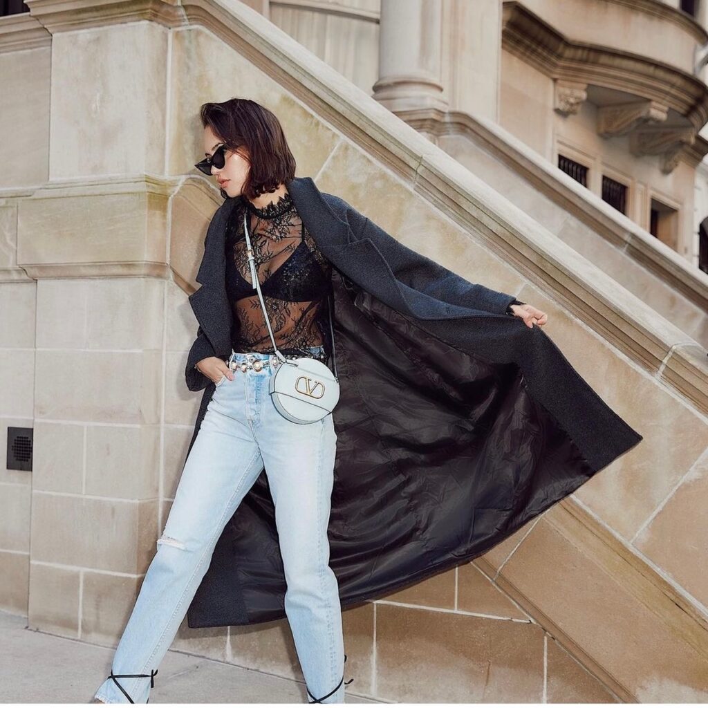 woman wearing a black lace top with light wash denim and a long black coat