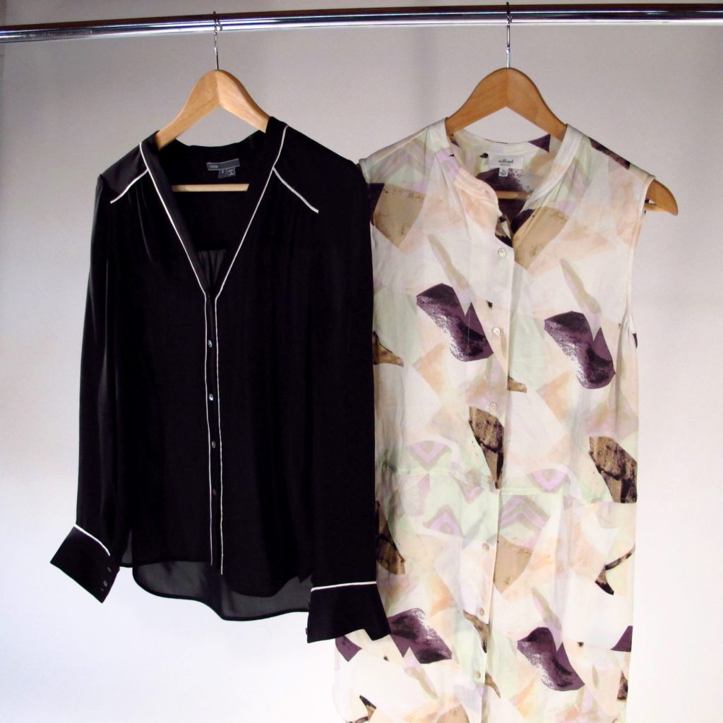 two silk blouses hanging on a rack, one black and one in a pastel feather print