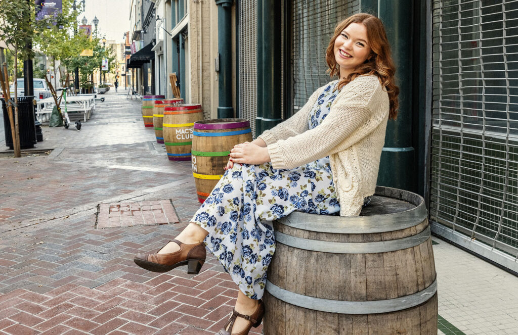 Model wearing a blue floral dress sitting on a wooden barrel